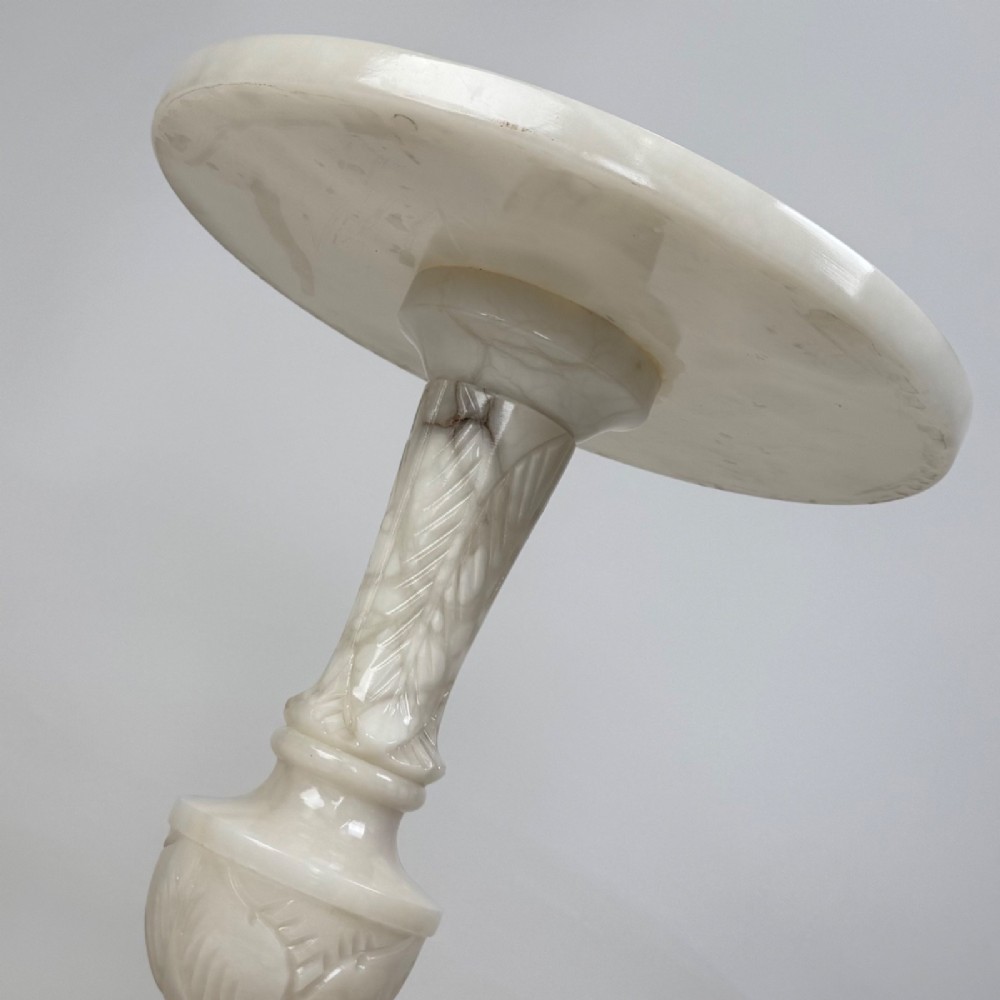 A carved white alabaster side table featuring a circular top resting on a decorative turned pedestal stem and round base. View VI