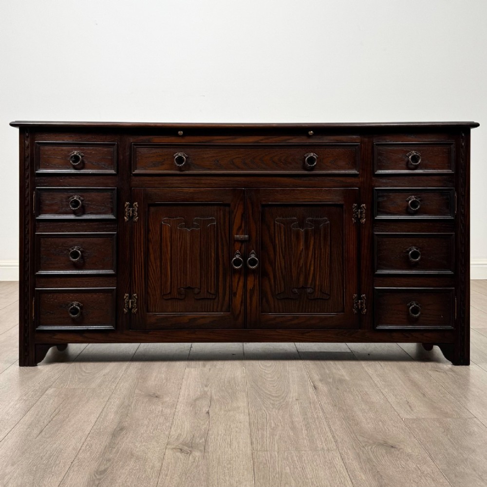 A dark oak sideboard featuring carved linenfold central doors flanked by eight drawers with metal drop ring handles.