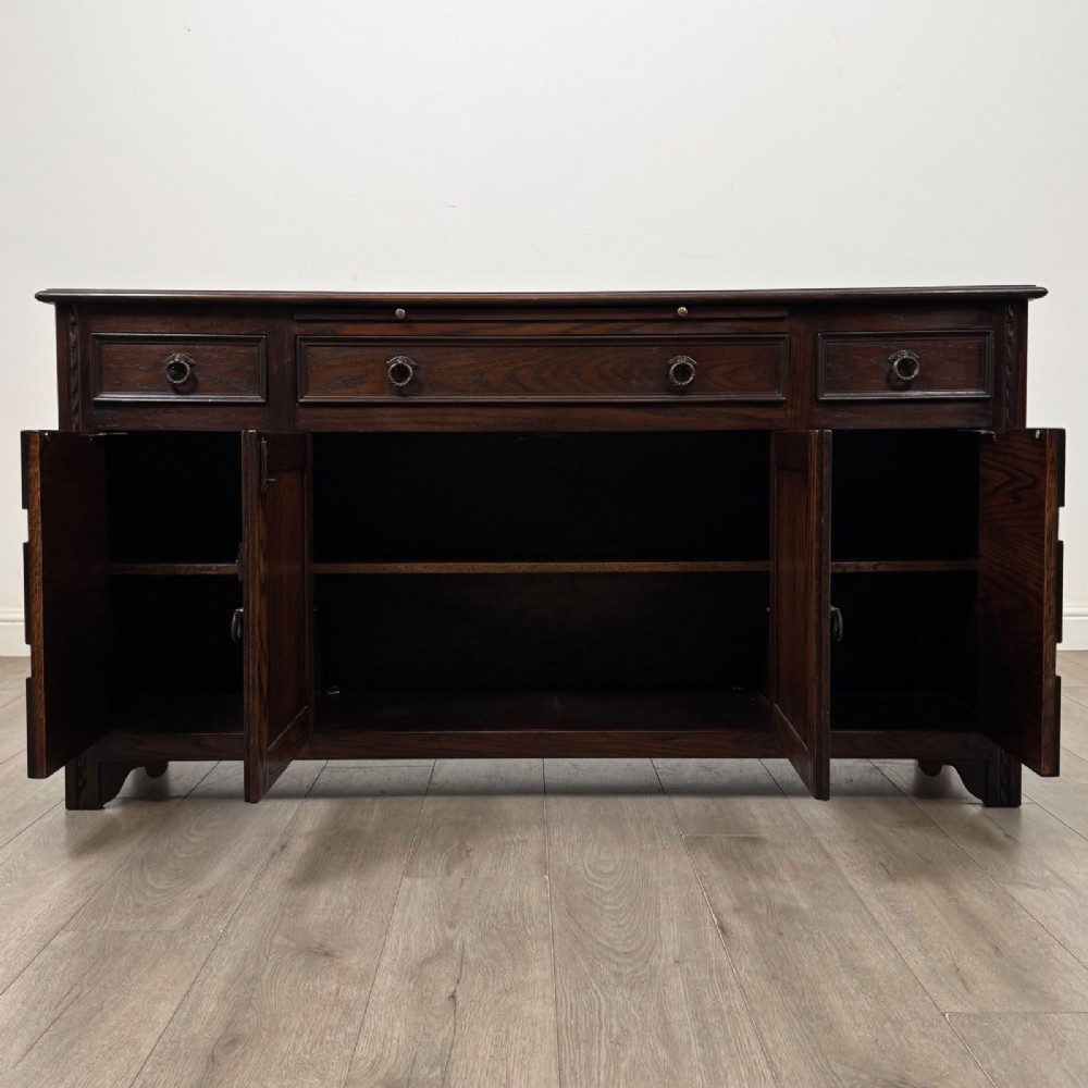 A dark oak sideboard featuring carved linenfold central doors flanked by eight drawers with metal drop ring handles. View II
