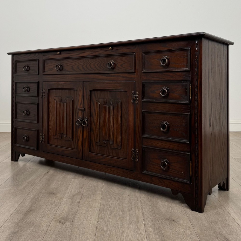 A dark oak sideboard featuring carved linenfold central doors flanked by eight drawers with metal drop ring handles. View III