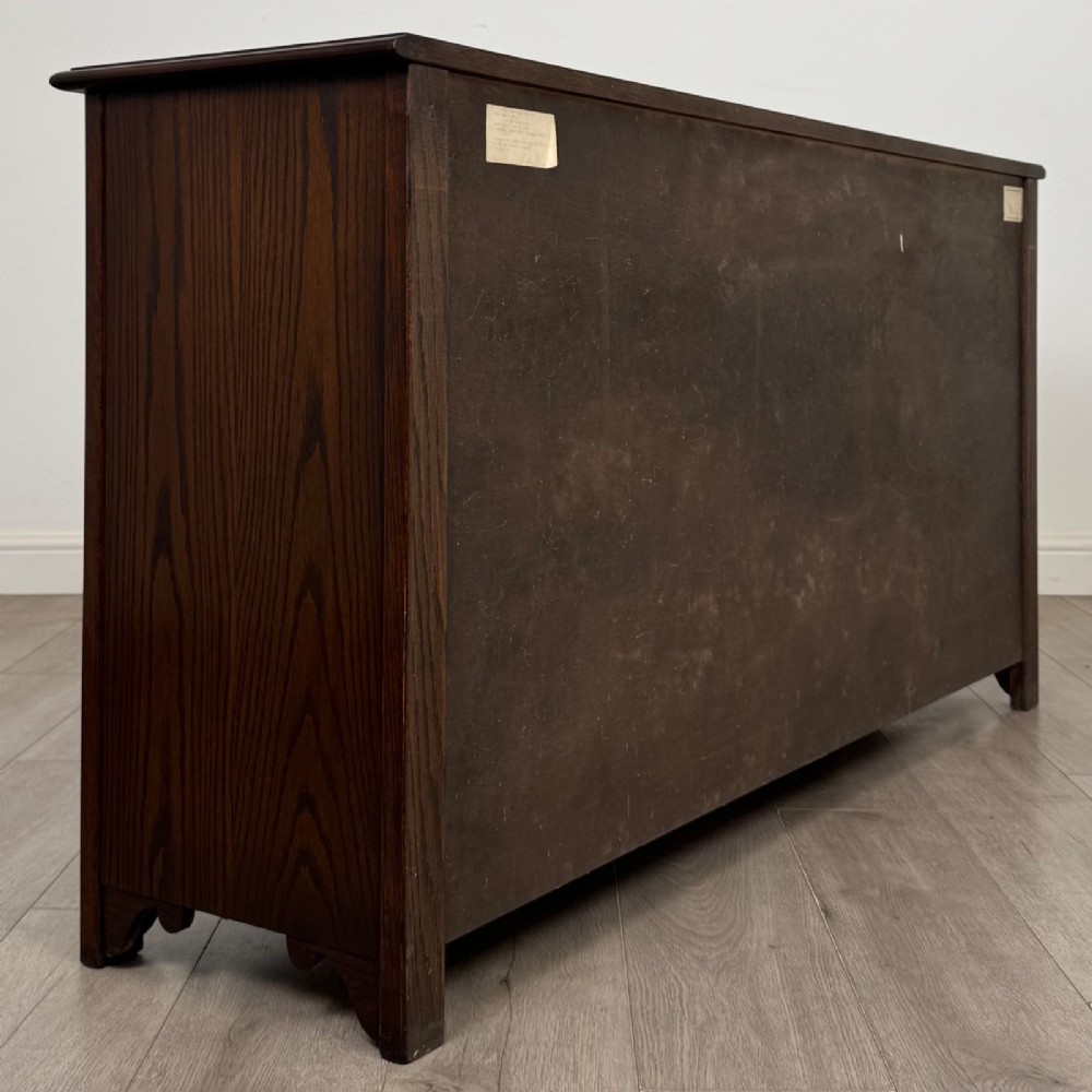 A dark oak sideboard featuring carved linenfold central doors flanked by eight drawers with metal drop ring handles. View V