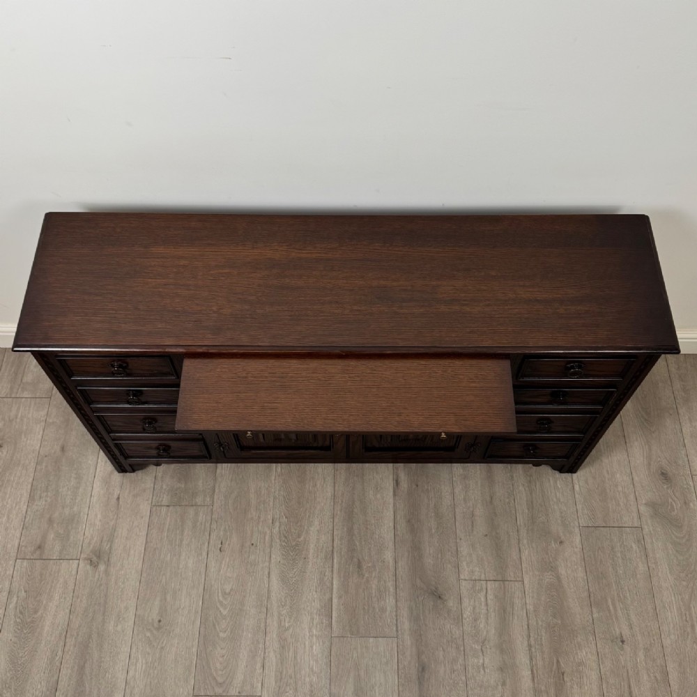 A dark oak sideboard featuring carved linenfold central doors flanked by eight drawers with metal drop ring handles. View XI