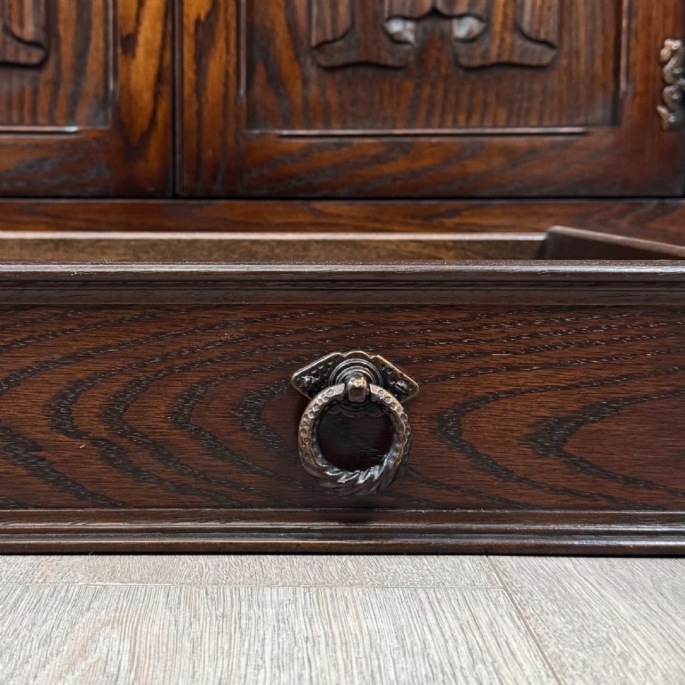 A dark oak sideboard featuring carved linenfold central doors flanked by eight drawers with metal drop ring handles. View XII