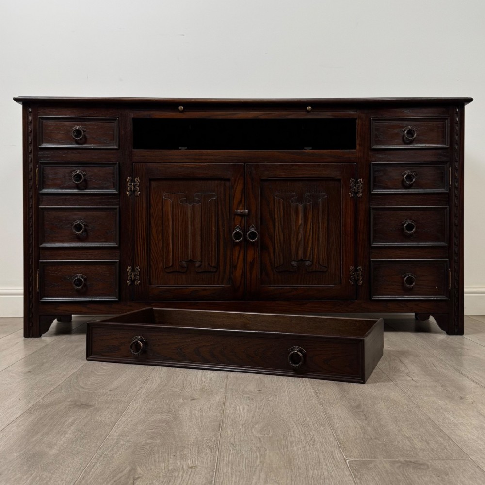 A dark oak sideboard featuring carved linenfold central doors flanked by eight drawers with metal drop ring handles. View XIII