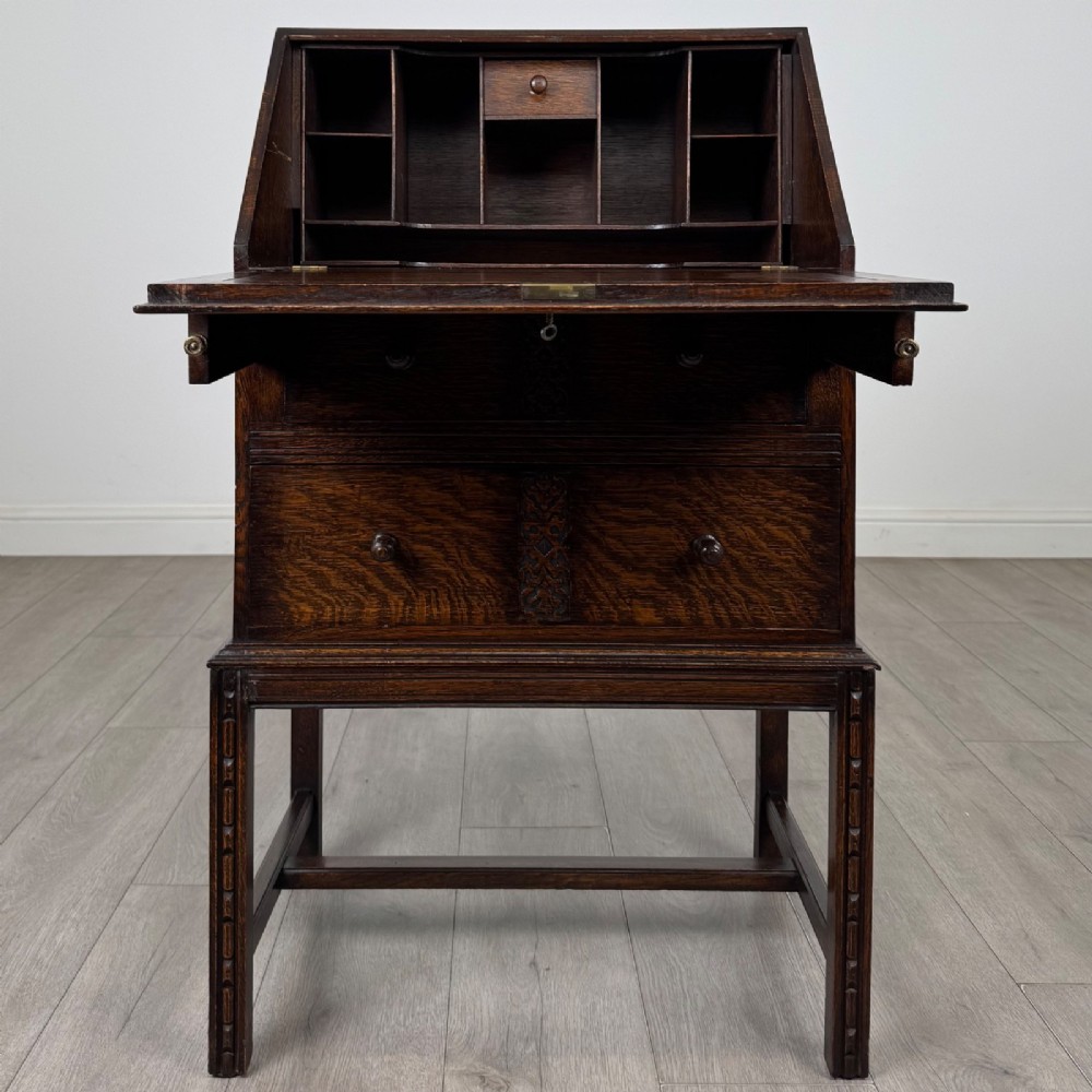 A small Edwardian dark oak writing bureau on a tall stand with two drawers featuring carved central panels and turned knobs. View II