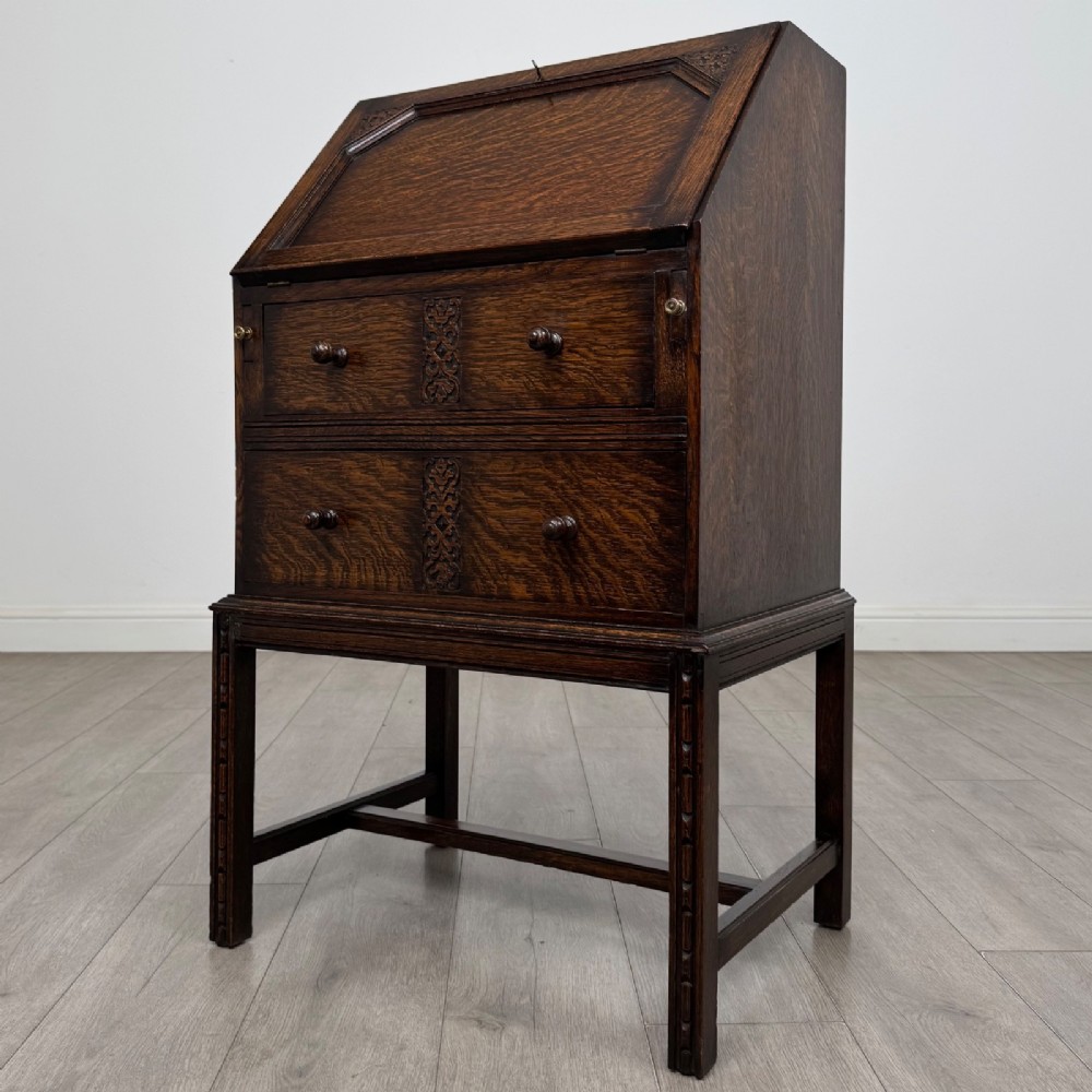 A small Edwardian dark oak writing bureau on a tall stand with two drawers featuring carved central panels and turned knobs. View III