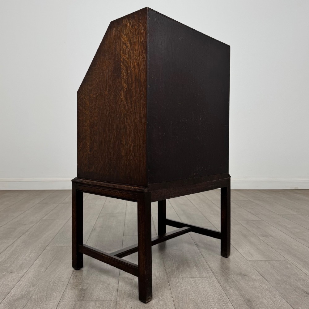 A small Edwardian dark oak writing bureau on a tall stand with two drawers featuring carved central panels and turned knobs. View V