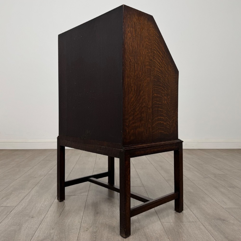 A small Edwardian dark oak writing bureau on a tall stand with two drawers featuring carved central panels and turned knobs. View VII