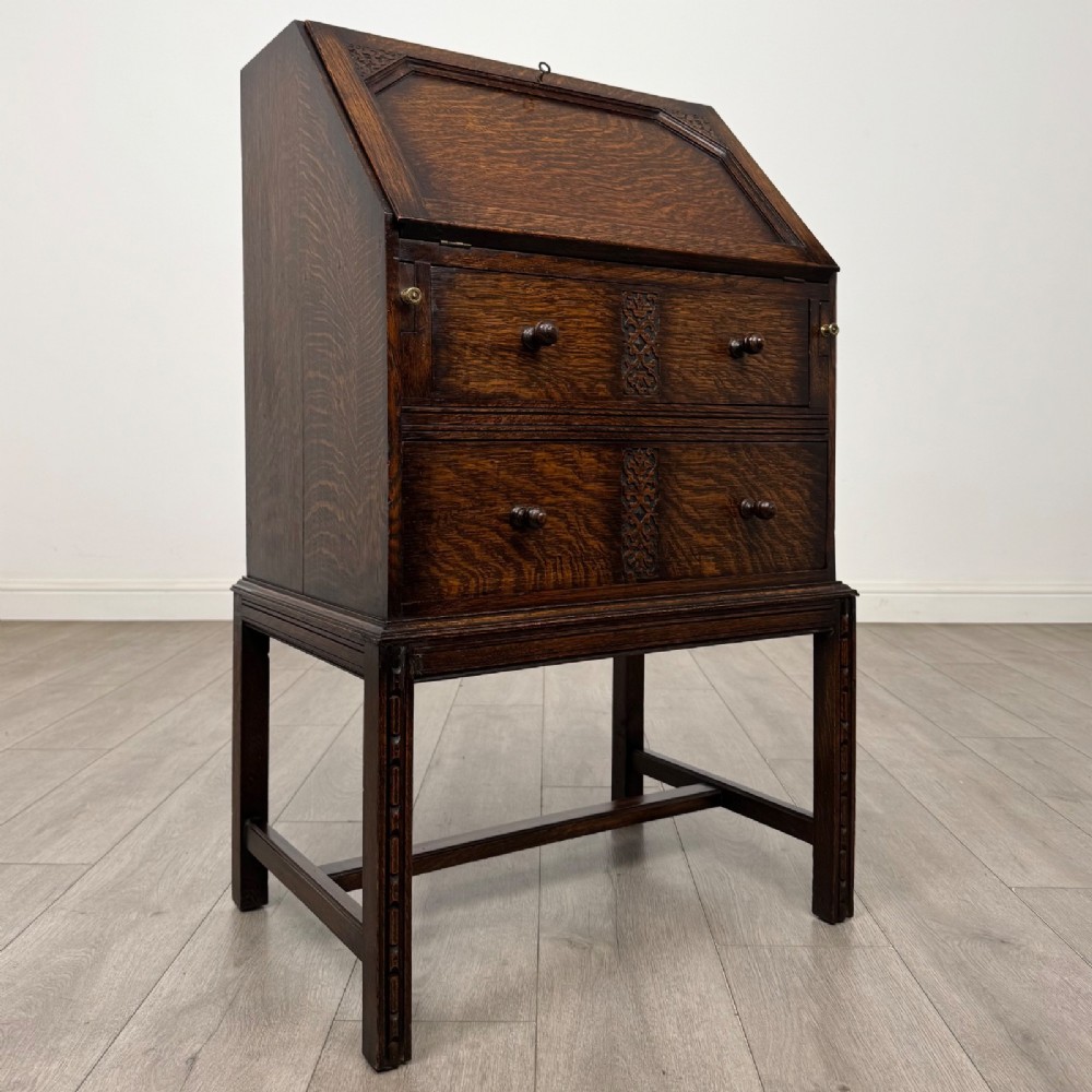 A small Edwardian dark oak writing bureau on a tall stand with two drawers featuring carved central panels and turned knobs. View IX