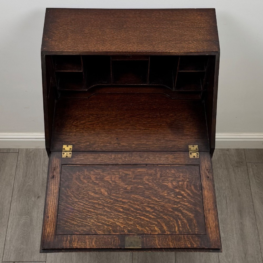 A small Edwardian dark oak writing bureau on a tall stand with two drawers featuring carved central panels and turned knobs. View XI