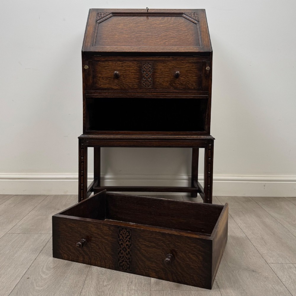 A small Edwardian dark oak writing bureau on a tall stand with two drawers featuring carved central panels and turned knobs. View XII