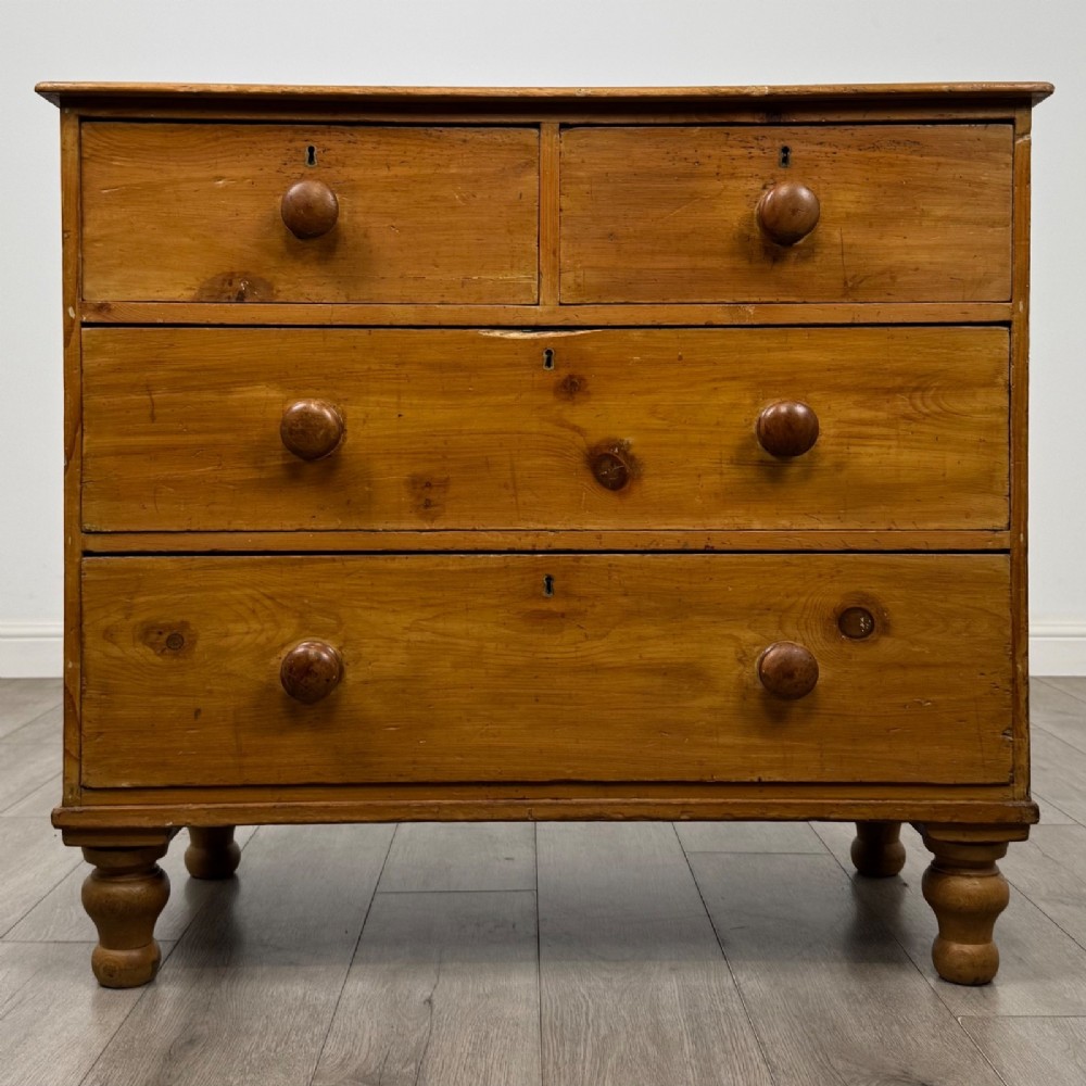 A Victorian pine chest of drawers featuring a two over two drawer layout, turned wooden knobs, and turned feet.