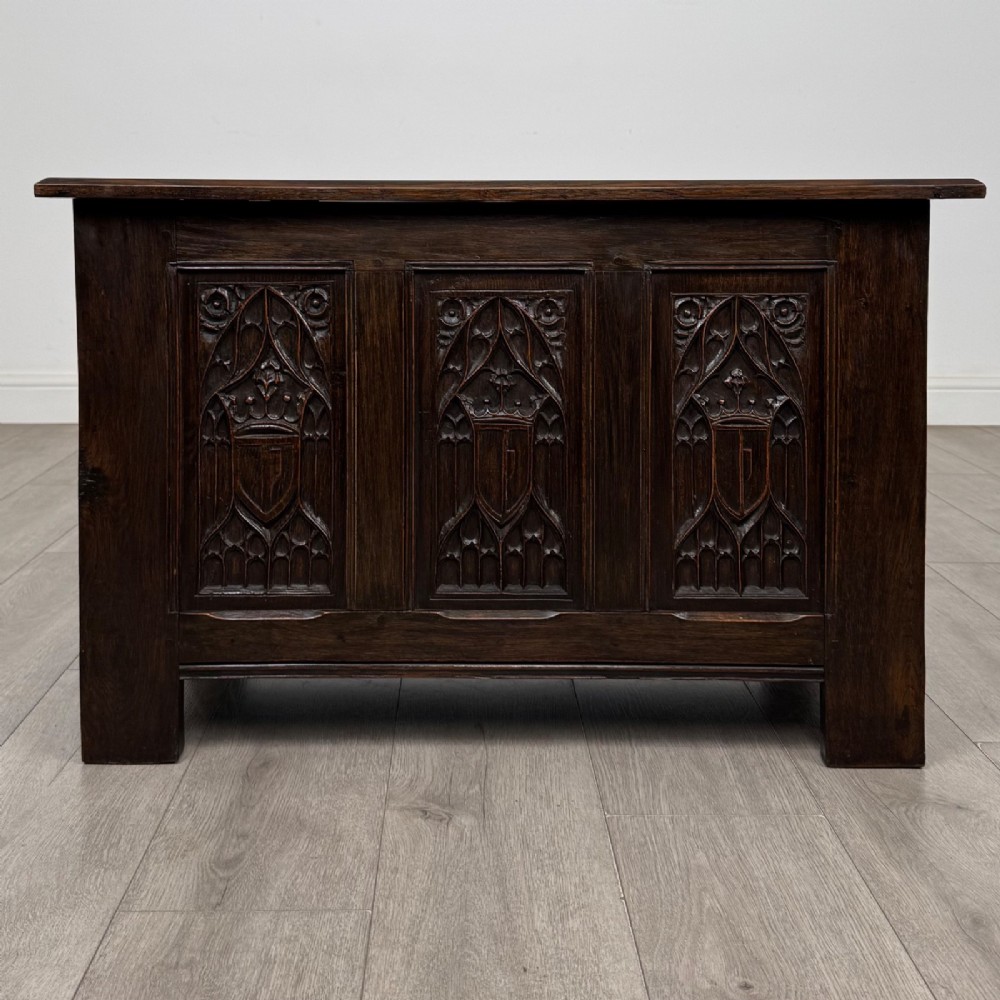 A dark oak blanket box featuring three front panels decorated with detailed Gothic arch and shield carvings.