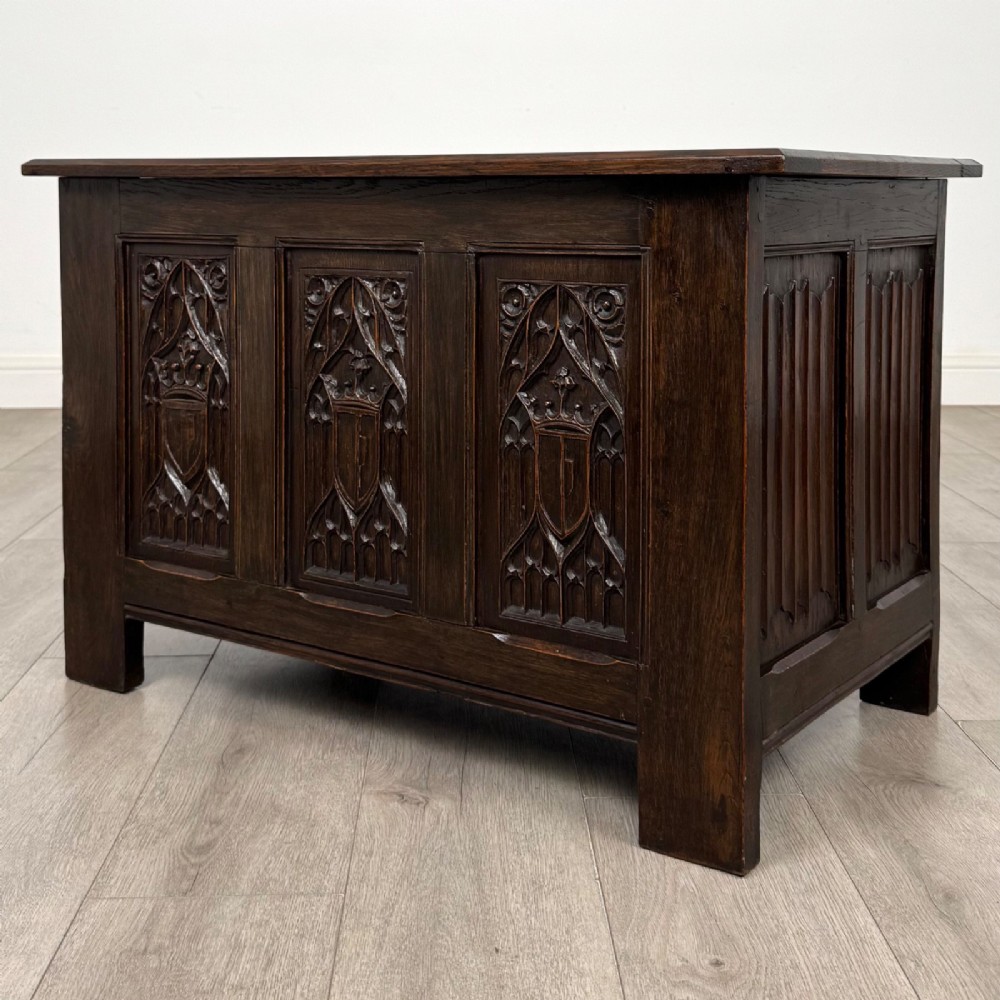A dark oak blanket box featuring three front panels decorated with detailed Gothic arch and shield carvings. View II