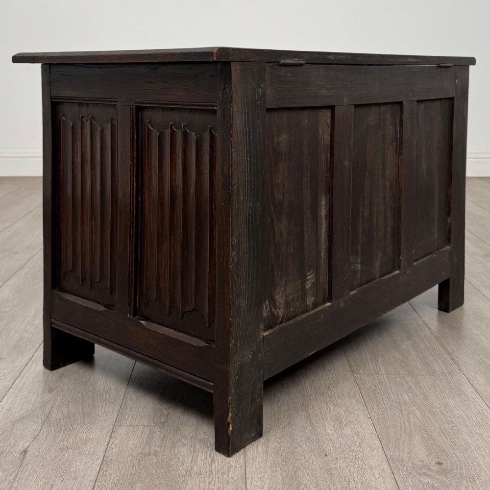 A dark oak blanket box featuring three front panels decorated with detailed Gothic arch and shield carvings. View IV