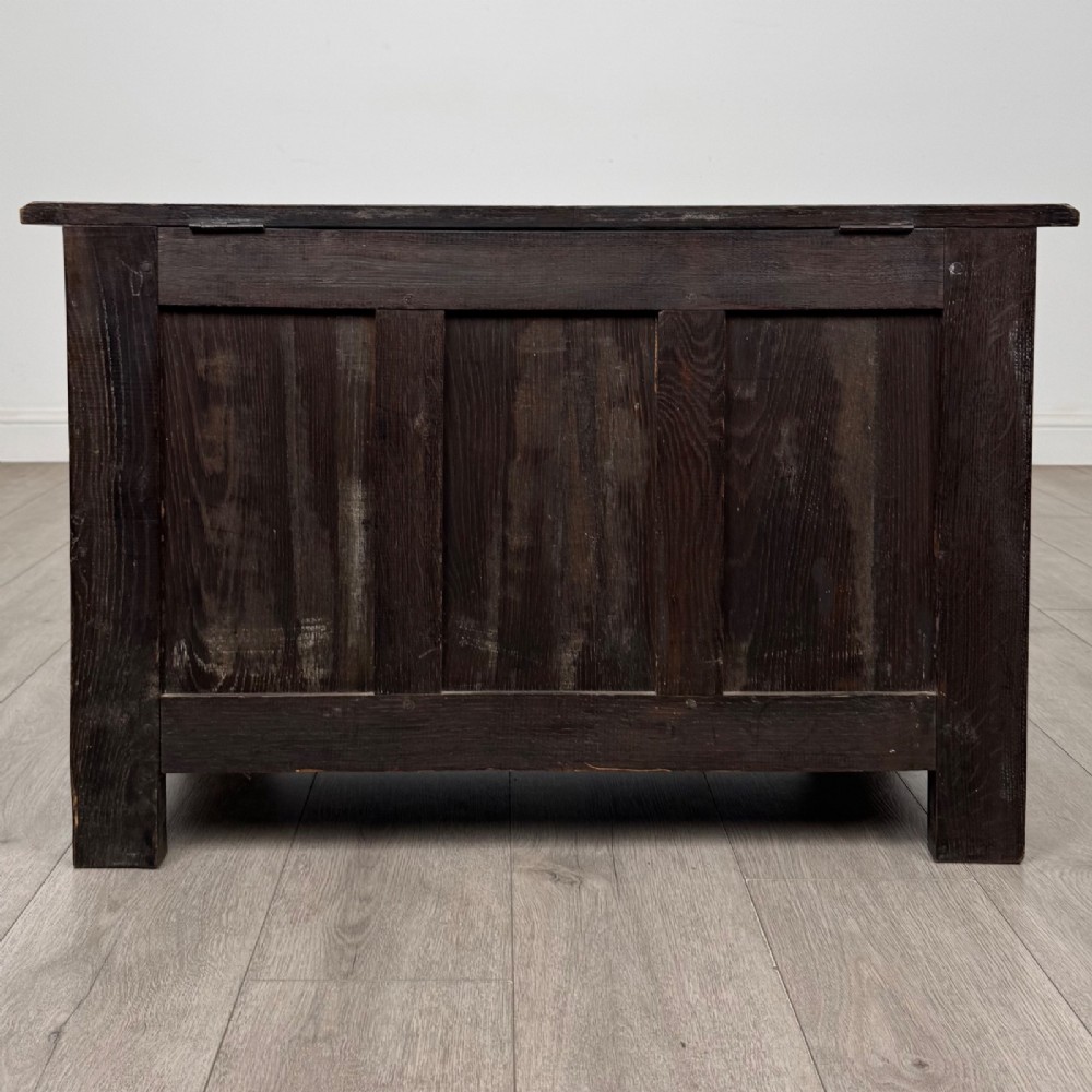 A dark oak blanket box featuring three front panels decorated with detailed Gothic arch and shield carvings. View V
