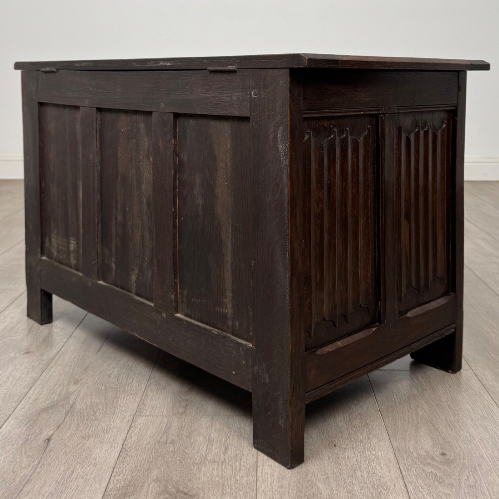 A dark oak blanket box featuring three front panels decorated with detailed Gothic arch and shield carvings. View VI