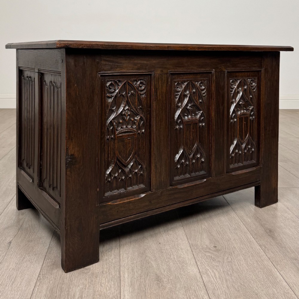 A dark oak blanket box featuring three front panels decorated with detailed Gothic arch and shield carvings. View VIII