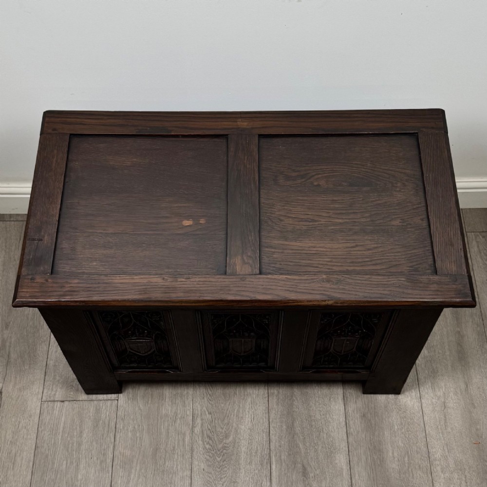 A dark oak blanket box featuring three front panels decorated with detailed Gothic arch and shield carvings. View IX