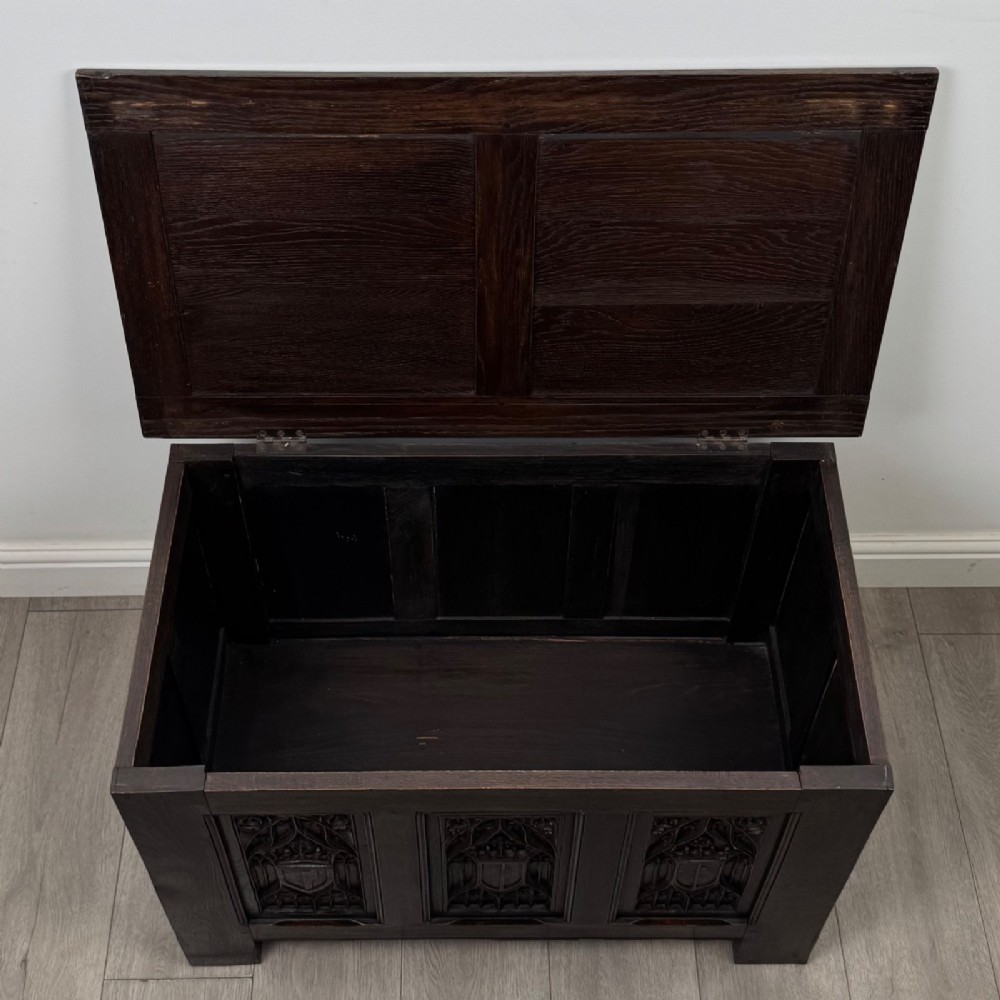 A dark oak blanket box featuring three front panels decorated with detailed Gothic arch and shield carvings. View X