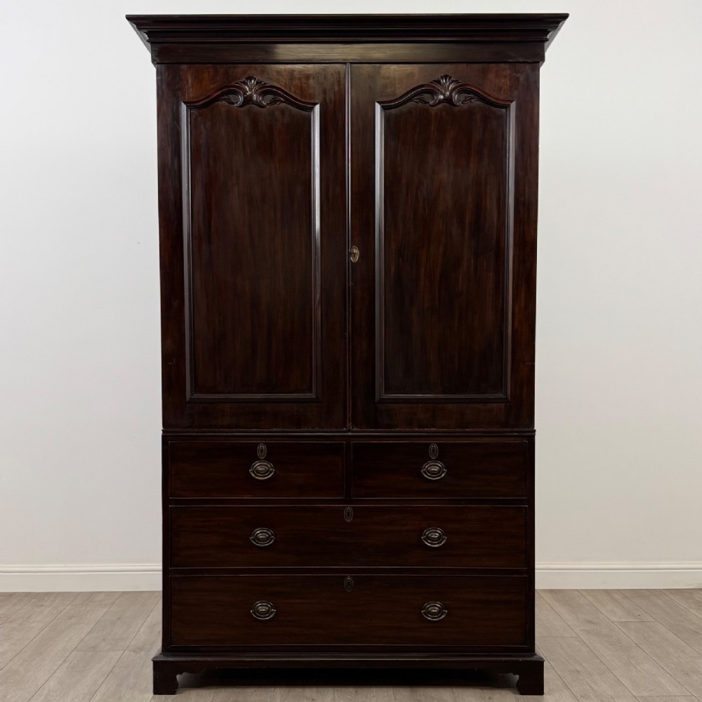 A tall 19th-century dark mahogany linen press featuring carved panelled doors on top and a chest of four drawers at the base.