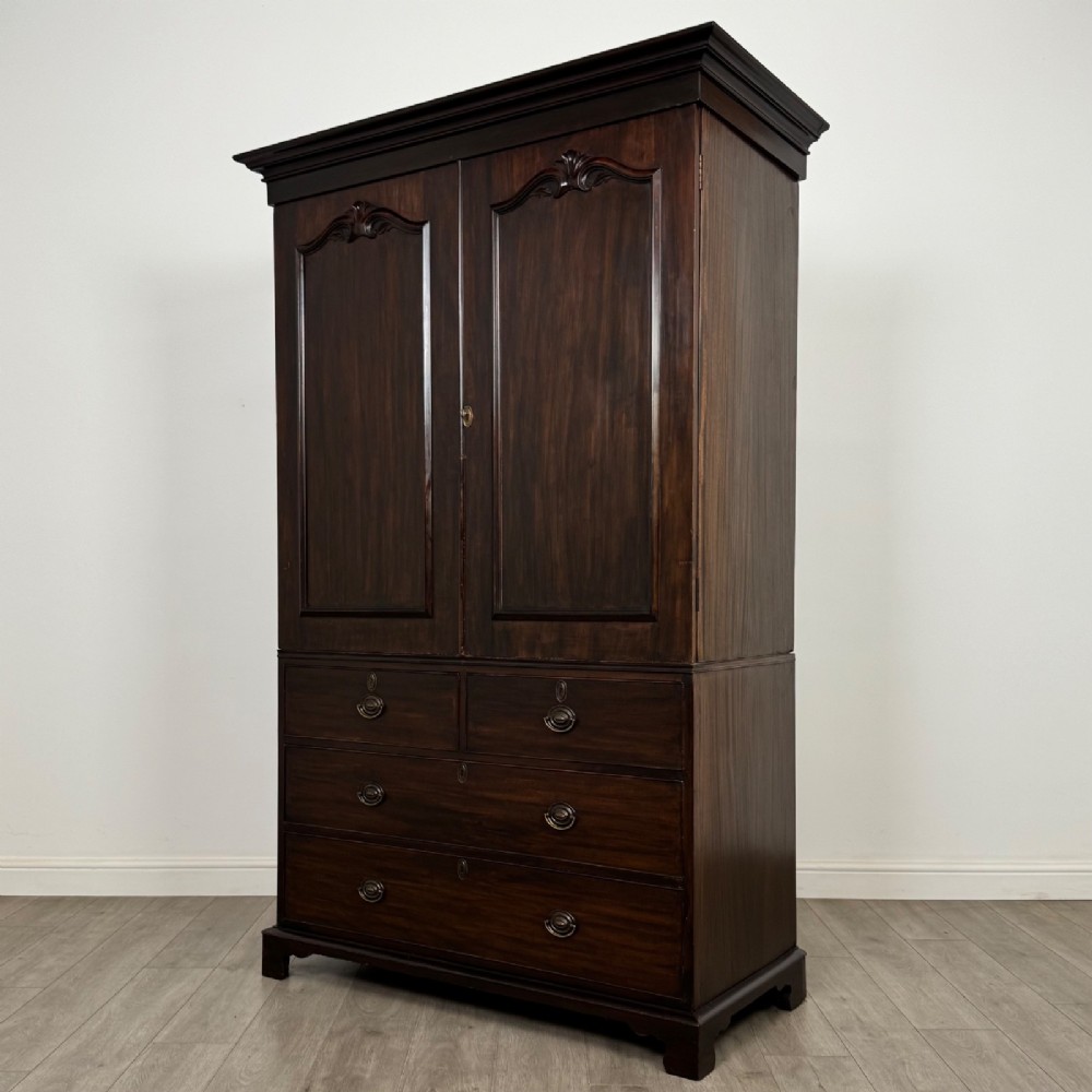 A tall 19th-century dark mahogany linen press featuring carved panelled doors on top and a chest of four drawers at the base. View III