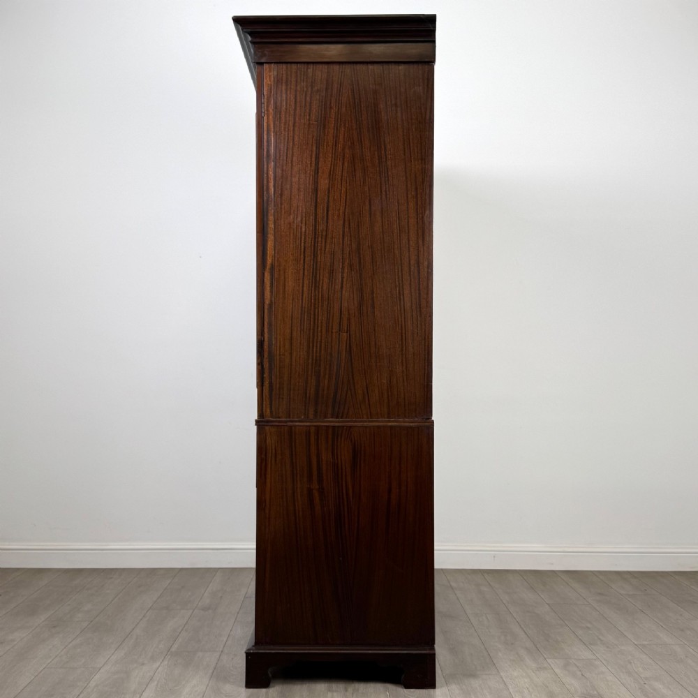 A tall 19th-century dark mahogany linen press featuring carved panelled doors on top and a chest of four drawers at the base. View IV