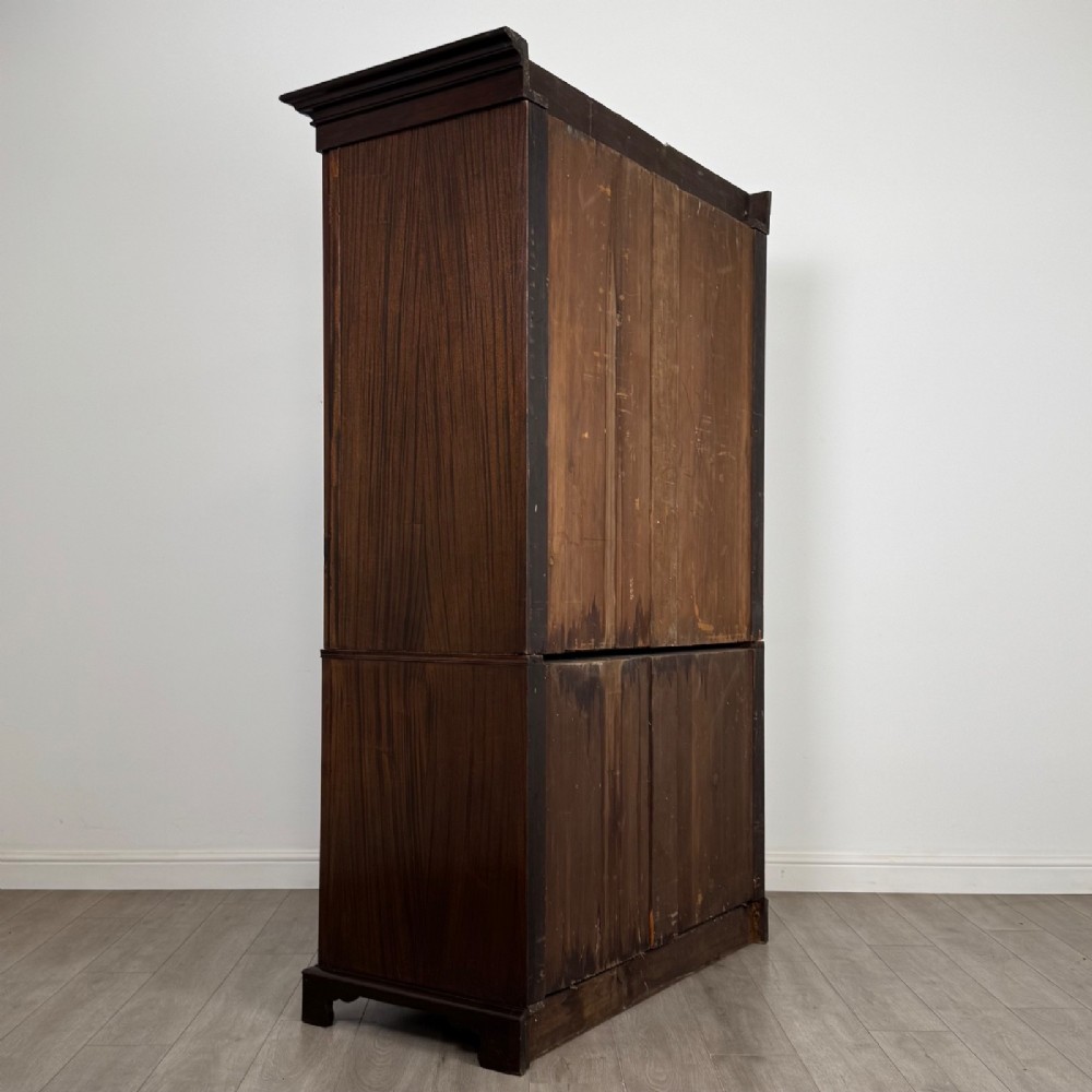 A tall 19th-century dark mahogany linen press featuring carved panelled doors on top and a chest of four drawers at the base. View V