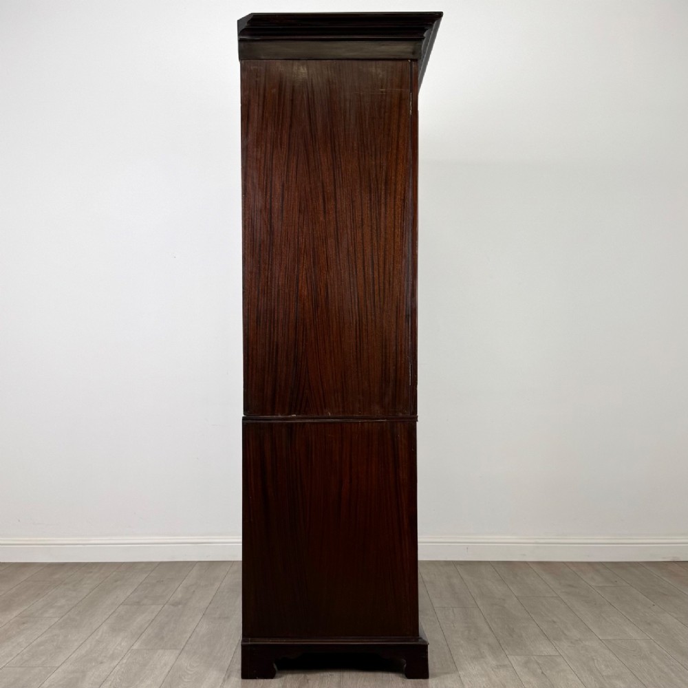 A tall 19th-century dark mahogany linen press featuring carved panelled doors on top and a chest of four drawers at the base. View VIII