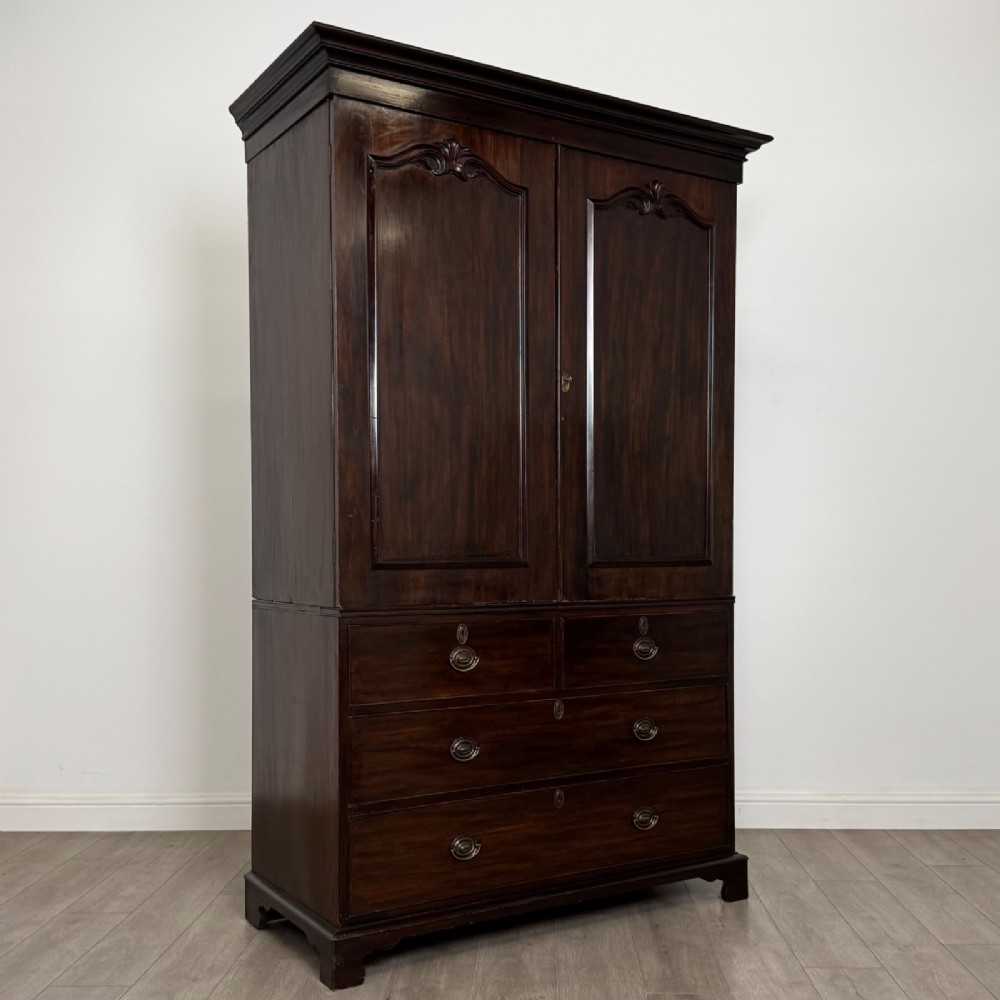 A tall 19th-century dark mahogany linen press featuring carved panelled doors on top and a chest of four drawers at the base. View IX