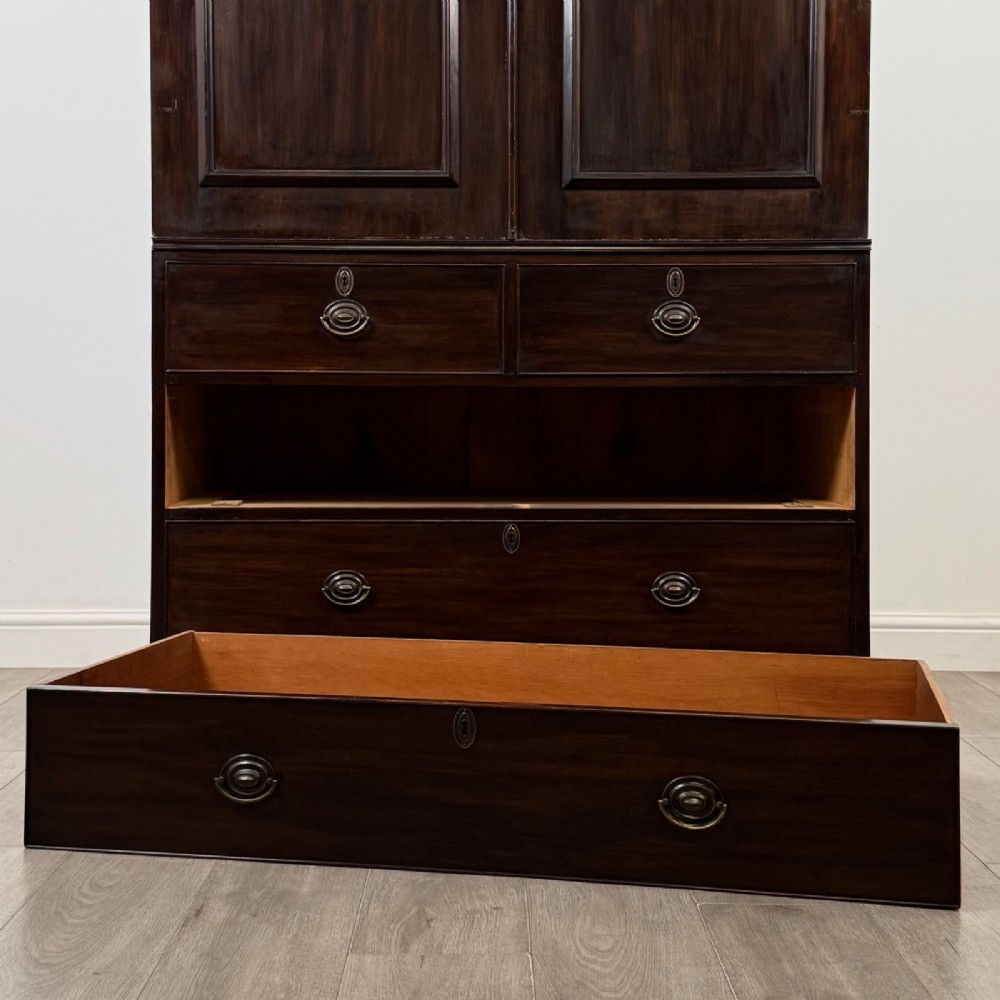 A tall 19th-century dark mahogany linen press featuring carved panelled doors on top and a chest of four drawers at the base. View X