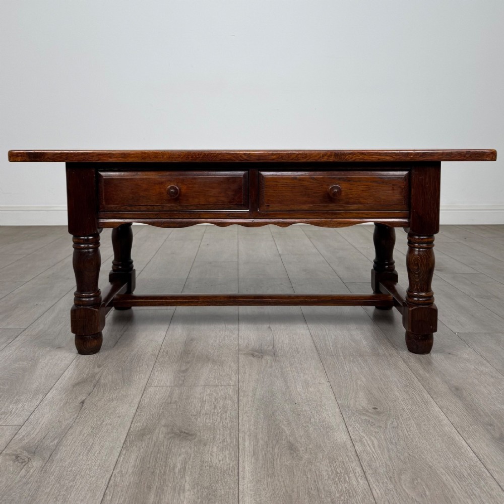 A dark oak rectangular coffee table featuring two front drawers with wooden knob handles and turned baluster legs connected by a low stretcher.