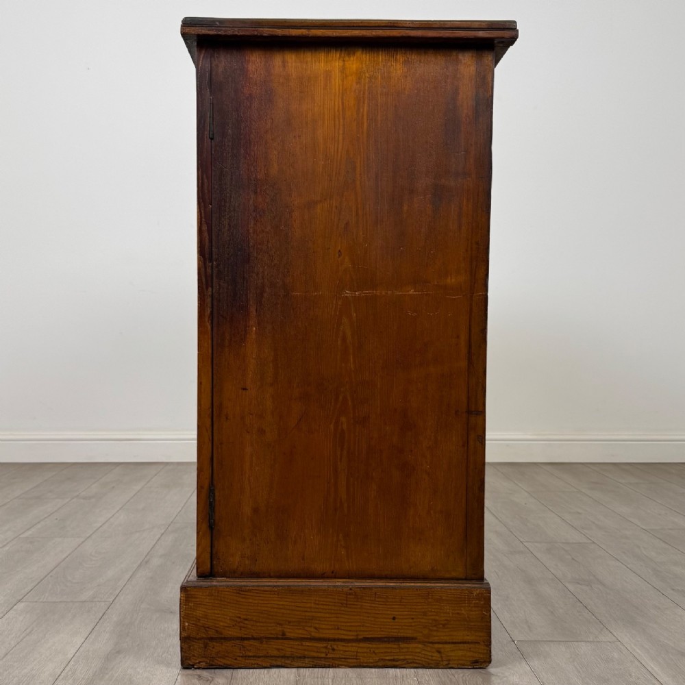 A nineteenth-century warm brown ash wood cupboard featuring four drawers on the left and a panelled cupboard door on the right resting on a plinth base. View IV