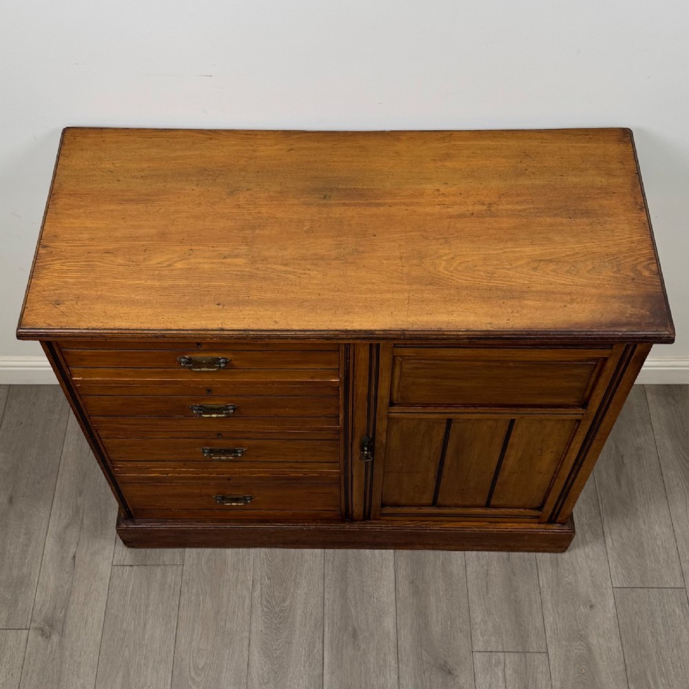 A nineteenth-century warm brown ash wood cupboard featuring four drawers on the left and a panelled cupboard door on the right resting on a plinth base. View X