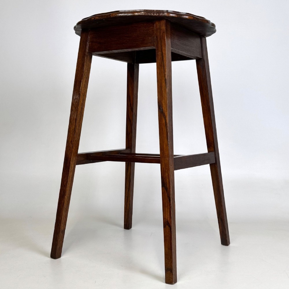 A tall, dark oak Edwardian side table featuring a scalloped piecrust rim top, four splayed square legs, and a lower slatted shelf. View IV