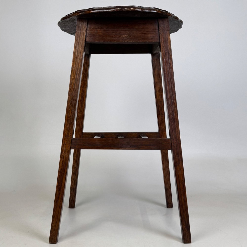 A tall, dark oak Edwardian side table featuring a scalloped piecrust rim top, four splayed square legs, and a lower slatted shelf. View V