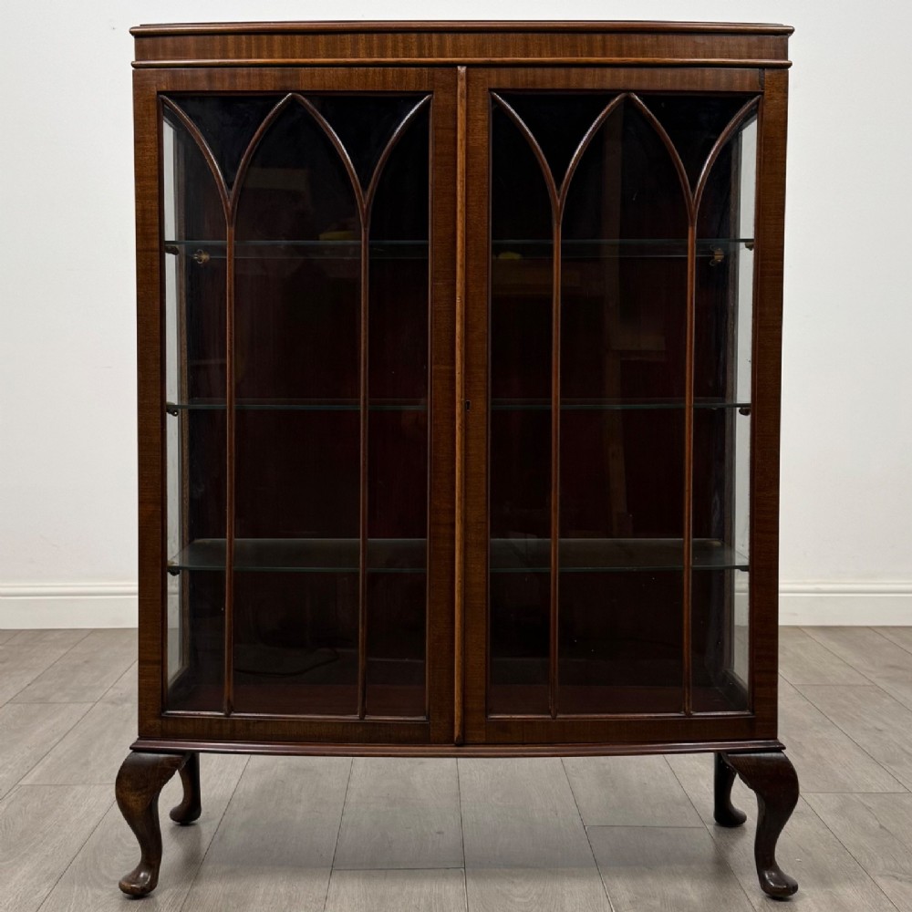 An Edwardian mahogany display cabinet featuring astragal glazed doors with gothic arches, interior glass shelves, and cabriole legs.