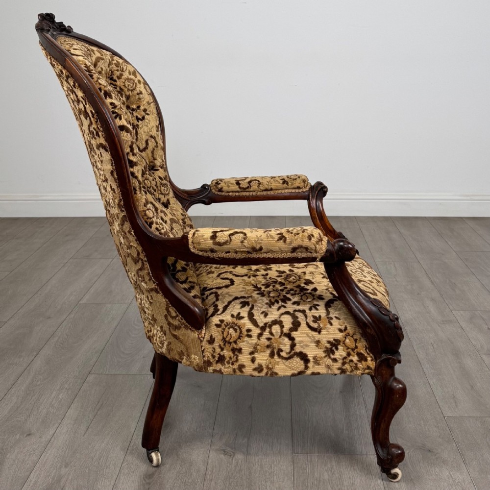 A 19th-century Victorian open armchair constructed from carved walnut wood and upholstered in a patterned gold and brown velvet fabric. View VI