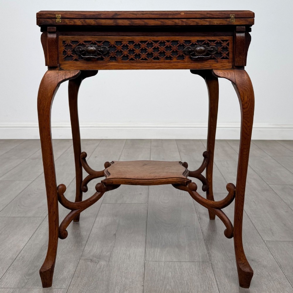 An Edwardian oak envelope card table featuring cabriole legs, a decorative carved drawer front, and a shaped lower shelf.