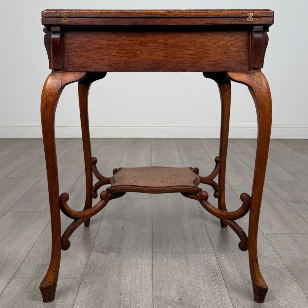 An Edwardian oak envelope card table featuring cabriole legs, a decorative carved drawer front, and a shaped lower shelf. View III