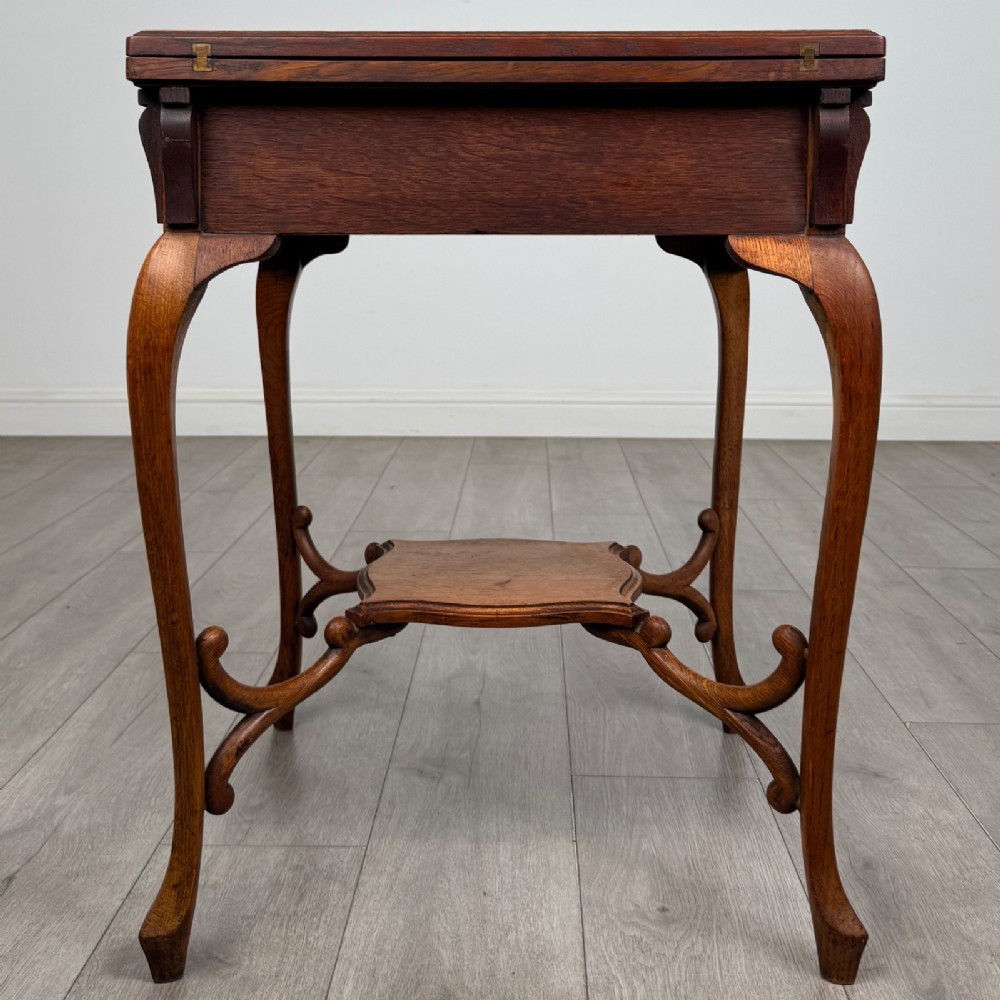 An Edwardian oak envelope card table featuring cabriole legs, a decorative carved drawer front, and a shaped lower shelf. View V