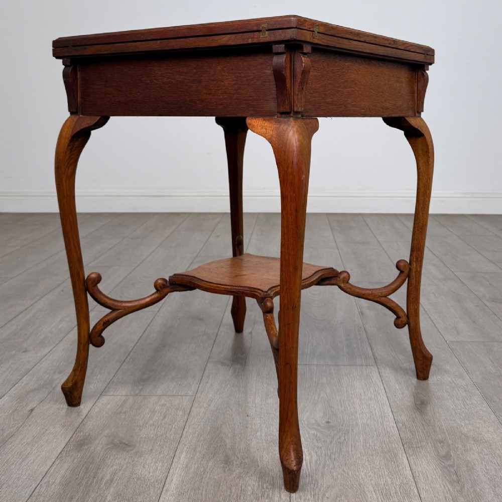 An Edwardian oak envelope card table featuring cabriole legs, a decorative carved drawer front, and a shaped lower shelf. View VI
