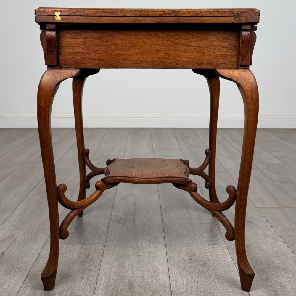 An Edwardian oak envelope card table featuring cabriole legs, a decorative carved drawer front, and a shaped lower shelf. View VII