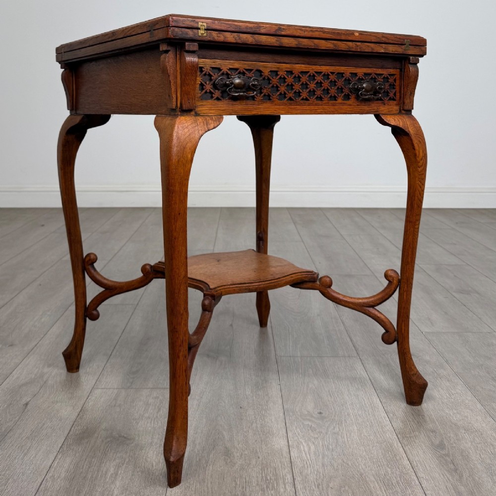 An Edwardian oak envelope card table featuring cabriole legs, a decorative carved drawer front, and a shaped lower shelf. View VIII