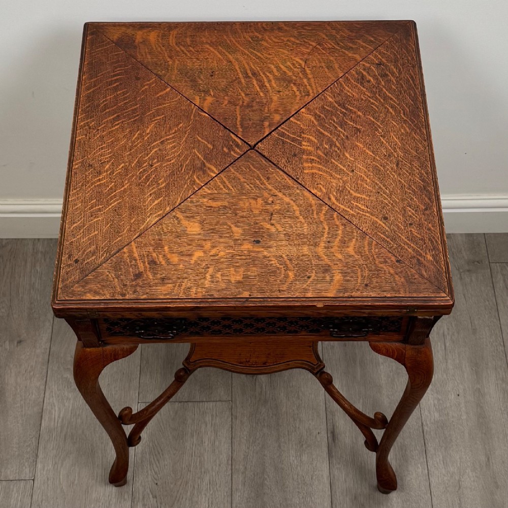 An Edwardian oak envelope card table featuring cabriole legs, a decorative carved drawer front, and a shaped lower shelf. View IX