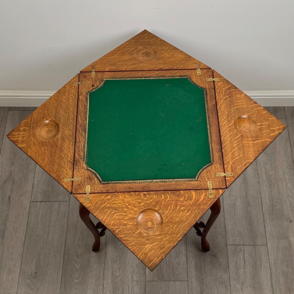 An Edwardian oak envelope card table featuring cabriole legs, a decorative carved drawer front, and a shaped lower shelf. View X