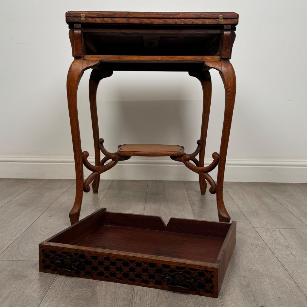 An Edwardian oak envelope card table featuring cabriole legs, a decorative carved drawer front, and a shaped lower shelf. View XI