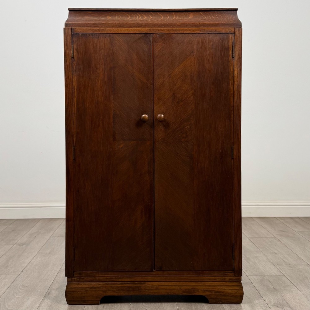 A compact 20th-century oak fitted wardrobe with two doors featuring diagonal grain veneering, turned wooden knobs, and a stepped top profile.
