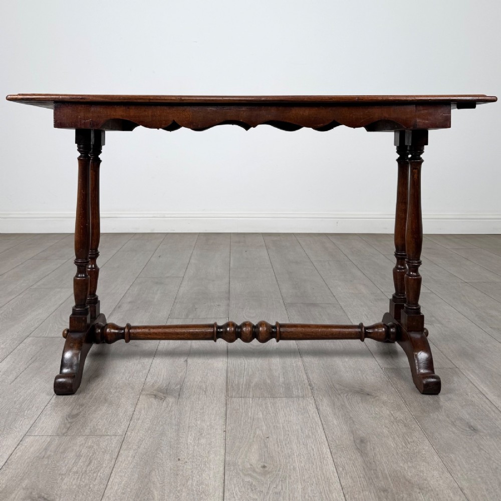 A 19th-century Victorian mahogany side table featuring a rectangular top with a scalloped apron, turned twin-column supports, a central turned stretcher, and curved feet. View V