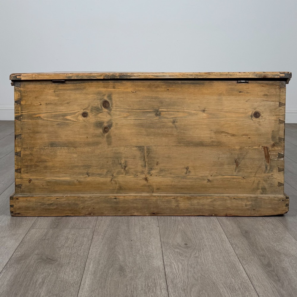 A rectangular nineteenth-century rustic pine blanket box with visible hand-cut dovetail joints, a central keyhole escutcheon, and a moulded base. View V